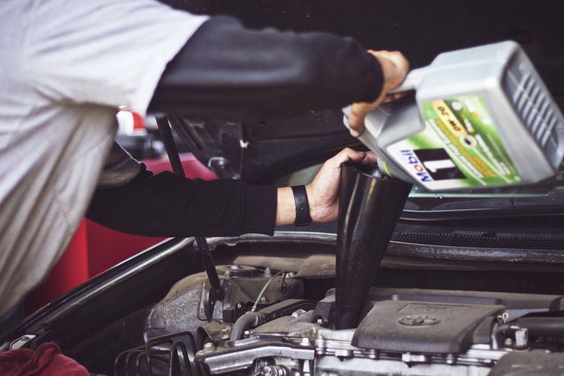 Uomo che rabbocca olio motore nel vano motore dell'auto